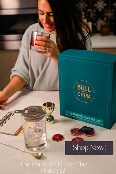 a woman sitting at a table holding a glass in front of a blue box with the words bull china on it