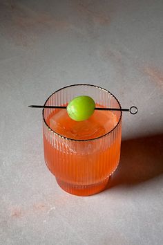 an orange cocktail with a green apple on the rim and a wire garnish