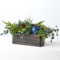 a planter filled with blue ornaments and greenery on top of a white table