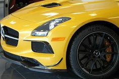 the front end of a yellow mercedes sls parked in a showroom with other cars behind it