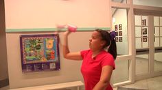 a woman holding up a pink object in front of a wall with pictures on it