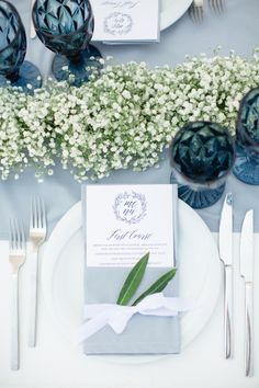 a place setting with blue and white plates, silverware and baby's breath flowers