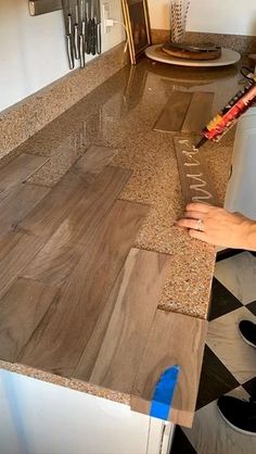 a person that is laying down some kind of tile on the counter in their kitchen