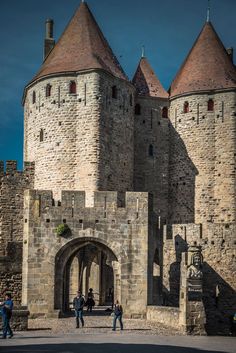 two people are standing in front of an old castle with stone walls and towers on either side