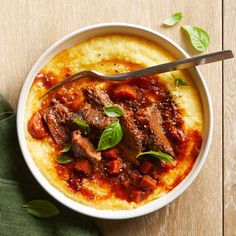 a white bowl filled with meat and vegetables on top of mashed potatoes next to a spoon