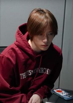 a young man sitting in front of a laptop computer wearing a maroon hoodie with the words, this university on it