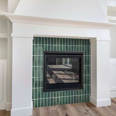 a fireplace with a green tile surround and wood flooring in a room that has white walls