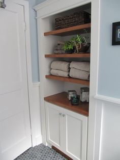 a bathroom with blue walls and shelving unit containing towels, potted plants and other items