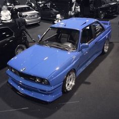 several cars are parked in a showroom with people looking at them and one car is blue