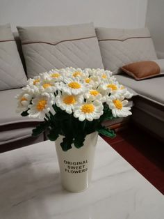 a white vase filled with yellow and white flowers on top of a marble coffee table