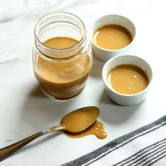 three small white bowls filled with caramel sauce and two spoons next to them