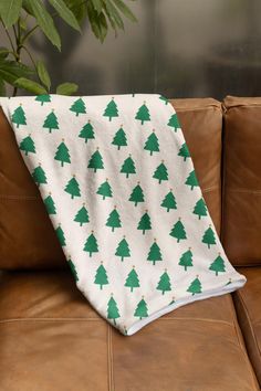 a white and green christmas tree blanket sitting on top of a brown leather couch next to a potted plant