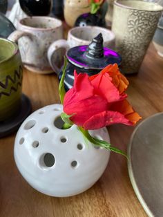 a red rose in a white vase on a table with other cups and saucers