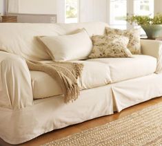 a white couch sitting on top of a hard wood floor next to a rug and window