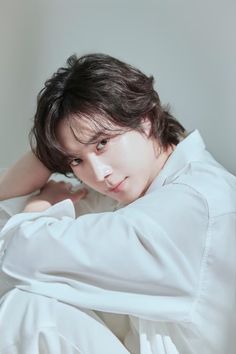 a young man in white shirt laying on the bed with his hands behind his head