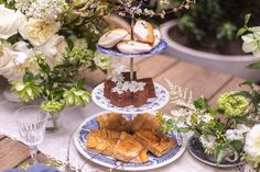 three tiered plates with pastries on them and flowers in vases next to each other