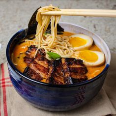 a bowl of ramen with chopsticks sticking out of the noodles and meat