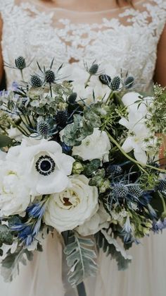 a bridal holding a bouquet of white and blue flowers with greenery on it