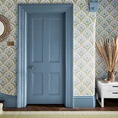 a blue door in front of a wallpapered room with a mirror and vase