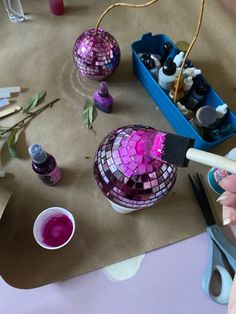 someone is painting some disco ball ornaments with pink and purple colors on the table next to them