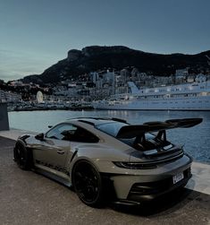 a grey sports car parked in front of a large body of water next to a city