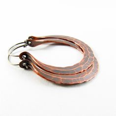 "Our medium large hammered copper Rio hoop earrings are earthy, rustic and beautiful, hand forged from large 10 gauge copper wire and oxidized for a deep glow. Fitted with standard 20 gauge sterling silver ear wires. Perfect for a weekend in Rio or anywhere an edgy punch to your wardrobe is needed! A great 7th anniversary jewelry gift. Earrings measure a touch under 2\" or 5.08cm long and 1.5\" or 3.81cm wide NOTE: Made To Order - Please Allow 3-5 business days for completion. The beauty of hand Rust Colored Hammered Copper Jewelry, Artisan Bronze Copper Hoop Earrings, Hoop Earrings Medium, Rustic Earrings, Mixed Metal Earrings, 7th Anniversary, Anniversary Jewelry, Large Hoop Earrings, Hammered Copper