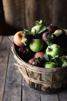 a wooden basket filled with lots of green and red apples on top of a wooden table