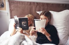 two women laying in bed while reading books