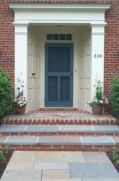 a blue front door with two potted plants on either side and steps leading up to it