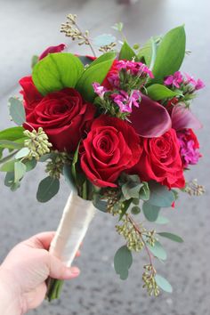 a person holding a bouquet of red roses and purple orchids in their left hand