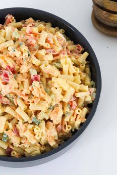 a black bowl filled with pasta salad on top of a white table next to some wooden slices