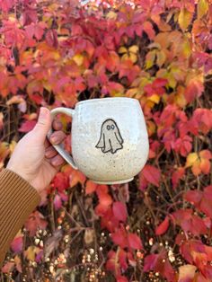 a person holding up a cup with a drawing on it in front of some bushes