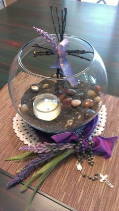 a glass bowl filled with rocks and candles on top of a wooden table next to a purple ribbon