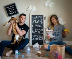 a man and woman sitting on the floor while holding a cat in front of them