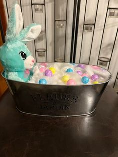 a stuffed rabbit sitting in a metal tub filled with candy eggs and cotton balls next to filing cabinets