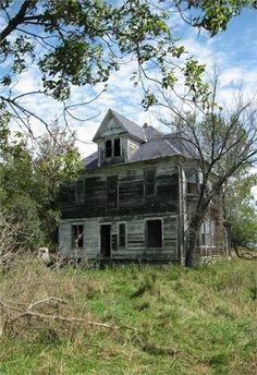 an old run down house sitting in the middle of a field with trees around it