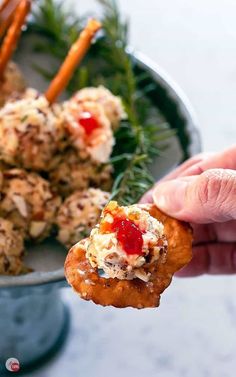 a hand holding up a cracker with crab salad on it and carrot sticks in the background