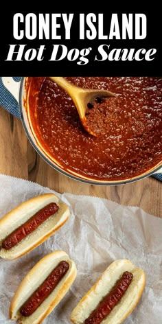 three hot dogs in buns with ketchup and mustard on the side next to a pot of chili