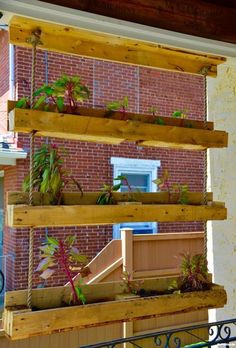 several wooden shelves with plants on them in front of a red brick wall and metal railing