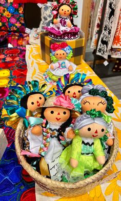 a basket filled with small dolls sitting on top of a colorful table cloth covered table