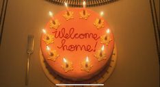 a welcome home cake with lit candles on the front and back of it that says welcome home