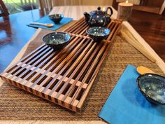 a wooden table topped with plates and bowls on top of a blue place mat next to a window