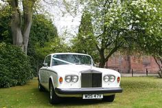 a white rolls royce parked in front of some trees