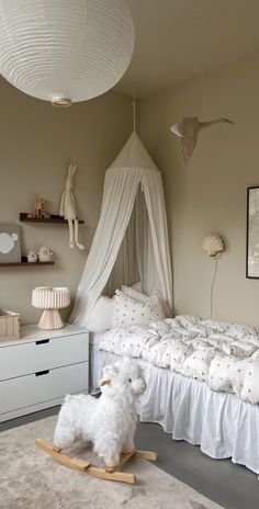 a white dog sitting on top of a bed next to a wooden rocking horse in a bedroom