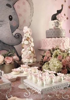 a table topped with cakes and flowers next to an elephant wall mural on the wall