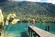 a man and a child are walking on a dock over the water with mountains in the background