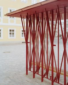 a red metal structure sitting on the side of a road next to a tall yellow building