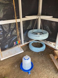 a tire swing sitting in the middle of a yard next to a blue plastic barrel