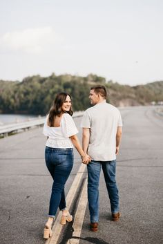 a man and woman holding hands while walking down the street with trees in the background