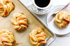 freshly baked pastries sitting on top of a pan next to a cup of coffee